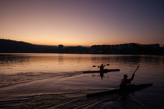 Silhouettes of kayakers paddling on a calm lake at sunset