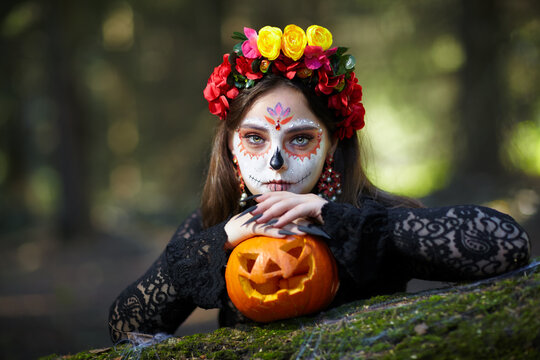 Halloween beauty portrait of young woman with Halloween pumpkin lies on a tree trunk in the forest.