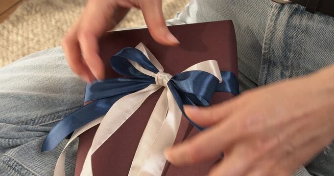 Woman hands adjusting blue and white satin ribbons bow on gift box close up video