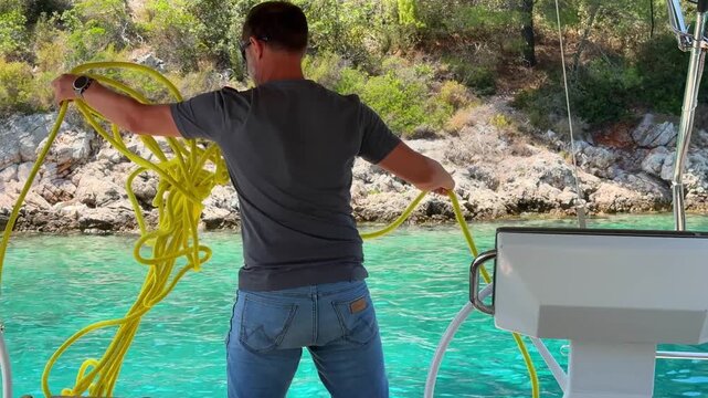 Man untangling mooring line on sailing yacht near Croatian coast. Preparing rope for mooring represents seamanship, boating and marine recreation