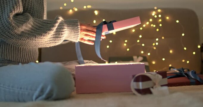 Woman hands opening gift box with glowing light inside looking into it on bokeh garland background close up video