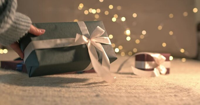Woman hand taking away green gift box with white satin ribbon on bokeh garland background close up video