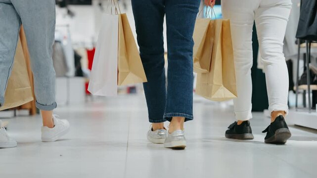 Low-angle view of three women walking through clothing store holding paper shopping bags, concept of movement and modern retail lifestyle