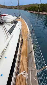 Woman walking along deck toward bow of sailing yacht near Croatian island. Camera tilting up from bare legs reveals boat bow and scenic Mediterranean coastline