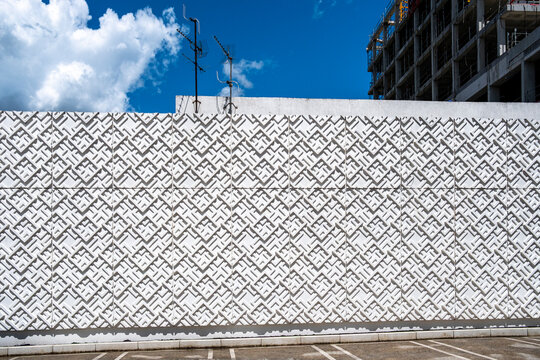 Patterned wall beneath blue sky creates an abstract architectural background with repeating geometric texture in a clean urban composition