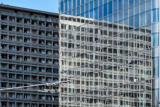 Reflective glass facade beside a concrete building creates an architectural pattern of urban reflections and repeated windows in a tight composition
