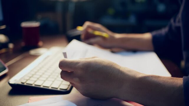 Close-up of a businessman checking financial data on clipboard documents and typing on a computer keyboard at his desk.