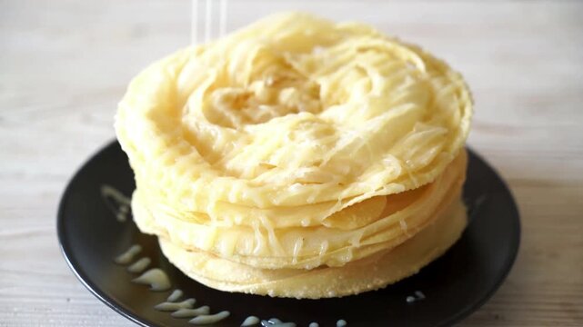 Stack of Crispy Layered Roti Bread Served on a Black Plate with Sweet Syrup Drizzle for a Delicious Traditional Breakfast