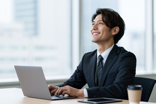 オフィスでパソコン作業する笑顔の日本人男性ビジネスマン未来への希望を感じる