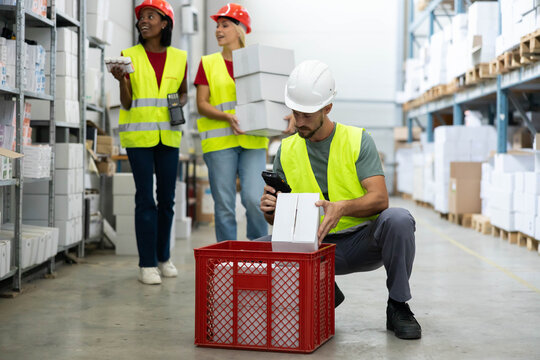 Diverse group of warehouse employees in safety vests and hard hats scanning barcodes and organizing products in a logistics facility