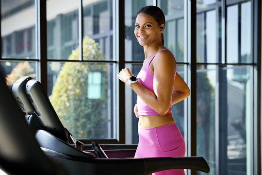 A woman runs on a treadmill. She smiles confidently while looking at camera. She feels energized and focused. Office in-house gym