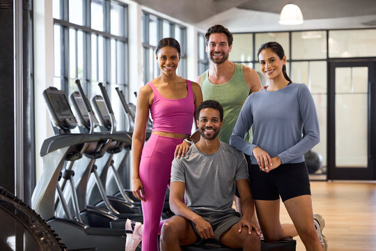 Four friends smiling together in a bright gym. They're posing confidently near treadmills, radiating joy and camaraderie. Office in-house gym