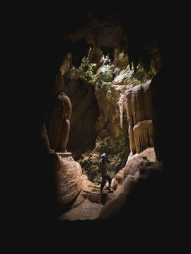 Adventurous Person Exploring Majestic, Naturally Lit Limestone Cave Formations in Southern Thailand.