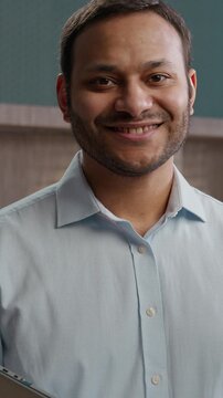 Joyful Indian Arabian business man smiling looking camera indoor office laptop workplace happy American businessman entrepreneur employer manager holding computer corporate portrait marketing company
