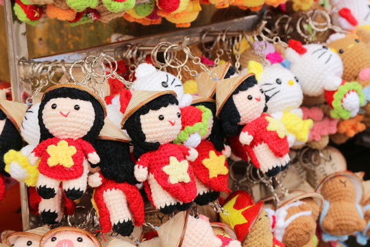 Handmade crocheted keychains shaped like traditional Vietnamese dolls wearing red ao dai dresses and conical hats displayed at a souvenir market in Hoi An, Vietnam.