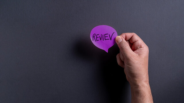 Person holds purple speech bubble with the word review written on it against black background while focusing on communication