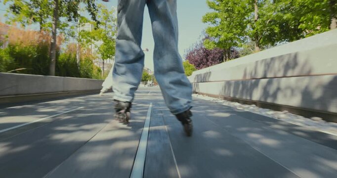 Two young women rollerblade along sunny park pathway as low tracking shot captures energetic movement. Friendship, urban fitness and active recreation concept.