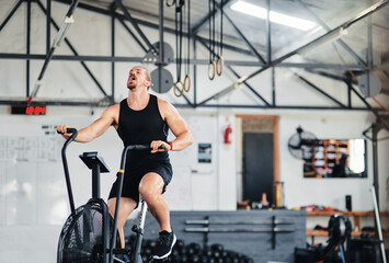 Fitness, man and tired with air bike in gym for cardio exercise, body workout or wellness...