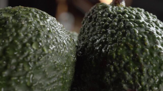 Extreme closeup of fresh green avocado showing rough bumpy peel texture, natural surface details and dark green skin with another avocado partially visible