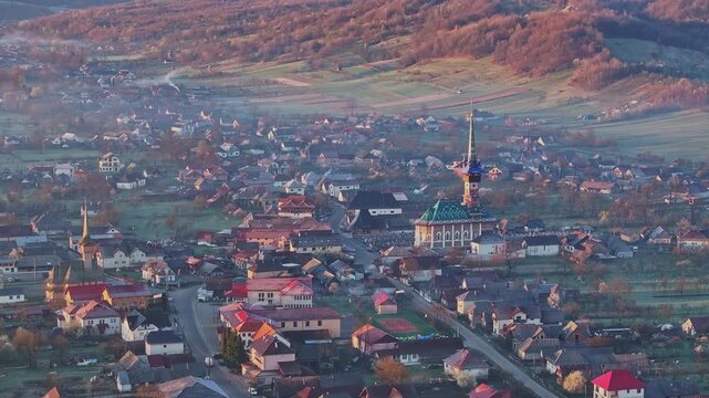 Aerial view of Săp&acirc;nța village on a misty morning, with traditional houses, church towers and forested hills in the rural landscape of Maramureș, Romania.