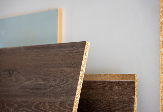 Laminated particleboard panels stored in a carpentry workshop, showing wood grain decor and exposed chipboard edges used for furniture, cabinetry and interior production.