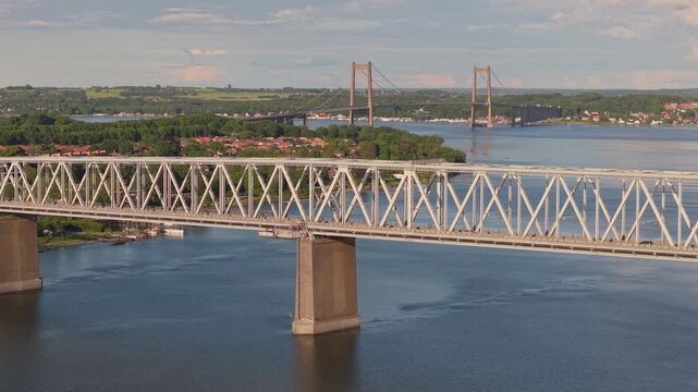 Lateral drone flight along the Old Little Belt Bridge in Middelfart as cars cross the bridge, revealing the New Little Belt Bridge on the horizon over the Little Belt Strait.