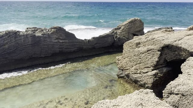 Dor Habonim Beach Nature Reserve, Zichron Yaakov, Israel. Top view of rocky formations in the Mediterranean Sea and the clear water between them. Foreground view through a pile of stones from the ruin