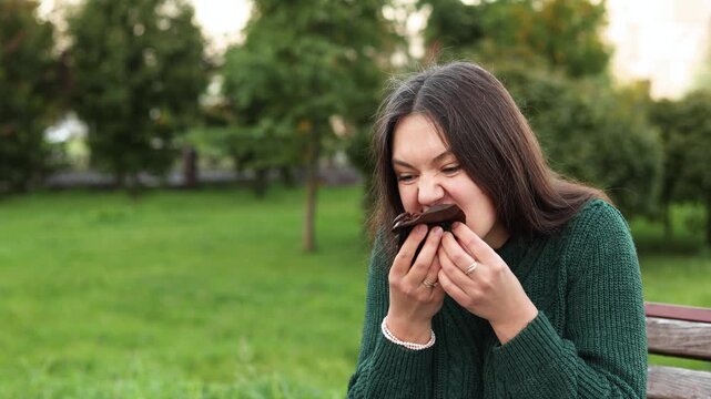 Woman eagerly unwraps chocolate cupcake and takes large bites. Slow motion reveals intense pleasure and emotional eating linked to stress and cravings.