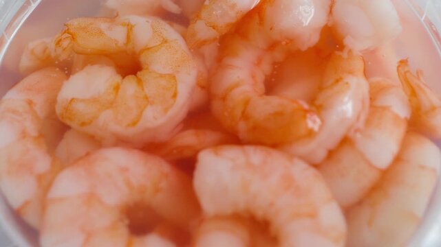 Close up of marinated shrimp in brine, showing cooked pink shrimp preserved in a seasoned liquid.