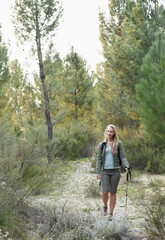 Obraz premium Woman in her thirties walking sandy trail in pine forest wearing olive jacket holding trekking pole