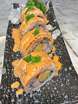 Delicious torched salmon sushi rolls with spicy mayo sauce and crab sticks inside, served on a black plate, traditional Japanese food.