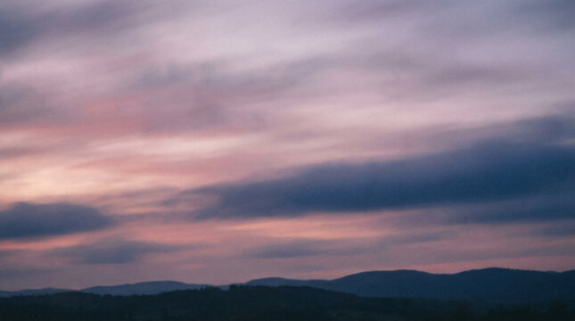 Dusk sky with soft pink and purple clouds over silhouetted rolling hills, peaceful twilight atmosphere, natural landscape vista