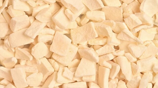 Rotating freeze-dried coconut cubes shot in macro close-up under bright studio lighting. Crisp white textured fruit pieces fill the full frame with detailed surface