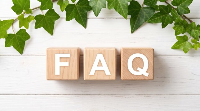Wooden toy blocks spelling the abbreviation FAQ for frequently asked questions with fresh green ivy leaves on a white wood board background symbolizing customer support and online help services