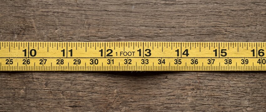 Yellow fabric measuring tape on a textured wooden background. Flexible ruler showing numbers and inches