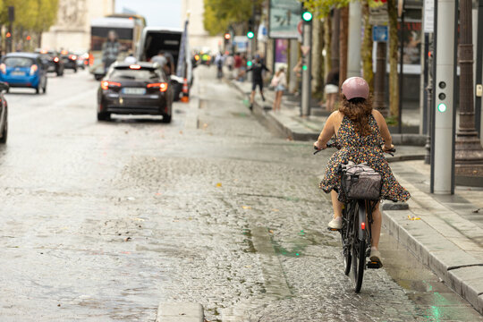 Woman cycling through busy city street on wet pavement, urban mobility, sustainable transportation, and everyday commuting