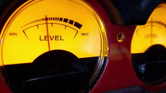 Glowing yellow retro VU meter displays audio signal fluctuations with an illuminated dial face. Ideal visual element for music production, sound engineering, and broadcast.