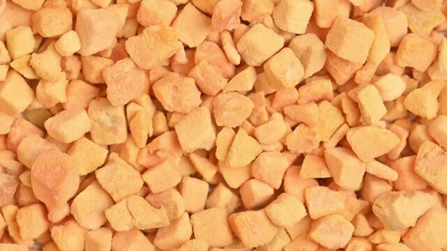 Rotating freeze-dried apricot pieces shot in top-down macro close-up under bright studio lighting. Crisp textured orange fruit pieces fill the full frame