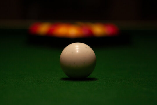 Close-up of white cue ball on green baize with blurred red and yellow racked pool balls behind