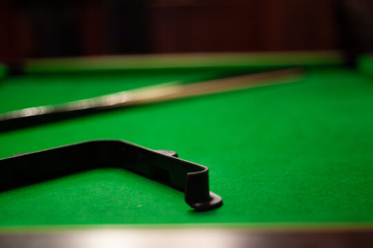 Atmospheric close-up of green felt pool table with black ball rack and blurred cue stick