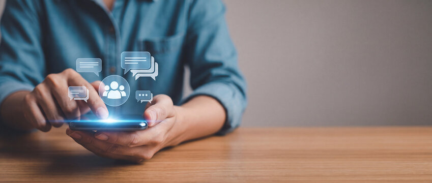 Close-up of a person's hands using a smartphone with glowing digital interface icons of speech bubbles and human avatars, representing social media networking, online communication and community.