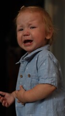 A distressed toddler with blonde hair crying while wearing a light blue button down shirt © Тарас Белецкий