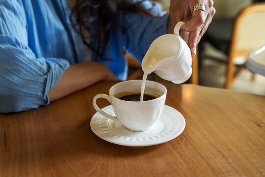 Close up of woman pouring fresh milk into coffee cup
