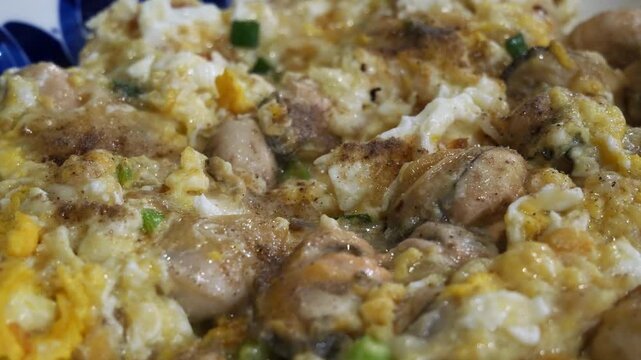 Thai oyster omelet with fresh oysters scrambled in fluffy egg and spring onion on blue and white porcelain plate, delicious seafood street food dish close-up