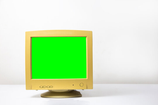 Vintage computer monitor with blank green screen on a white wall background with space for text.