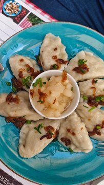 Plate of dumplings arranged in a circular pattern with a small bowl of apple sauce in the center, garnished with chopped herbs on a blue ceramic dish