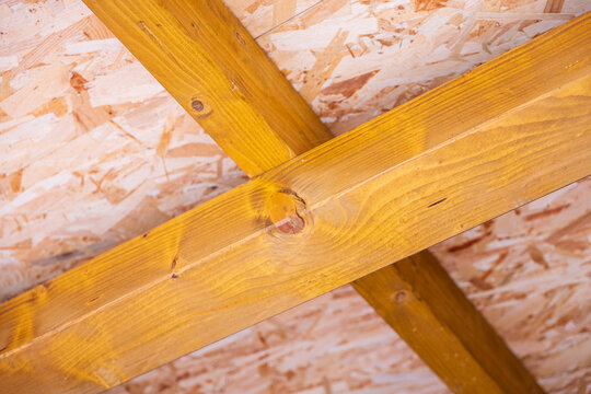Close-up of a wooden roof or ceiling structure with stained timber beams and OSB sheathing, showing structural framing, wood grain and engineered panels in building construction.