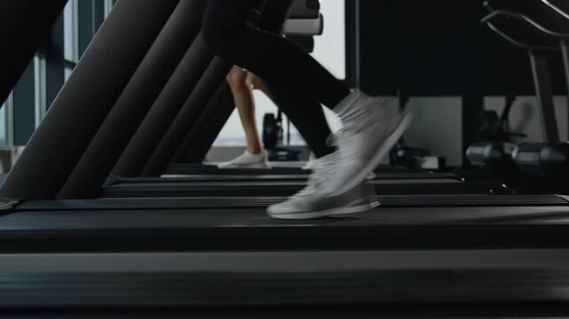 Close up female legs running on treadmill in fitness gym sports shoes jogging run jog cardio workout athletic sportswoman runner moving feet fast interval training healthy lifestyle exercise indoors