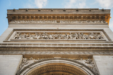 Low angle view of a classical building facade featuring ornate stonework, decorative cornices and symmetrical architectural elements against a blue sky. © Anastasia
