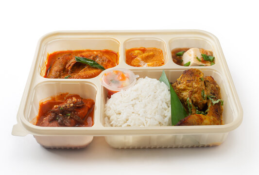 Malaysian bento lunch box with curry prawns, spiced chicken, tofu, and white rice isolated on white background high angle view